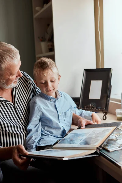 Abuelo y nieto en el sofá en casa. Abuelo y niños viendo fotos viejas —  Fotos de Stock