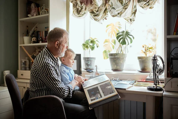 Dědeček a vnuk jsou doma na gauči. Děda a děti se dívají na staré fotky — Stock fotografie