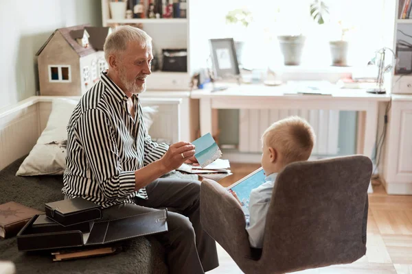 Dědeček vypadá fotoalbum se svou svatbou, chlapeček s elektronickým tabletem — Stock fotografie