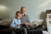 Großvater und Enkel nutzen digitales Tablet im Sitzen auf der Couch