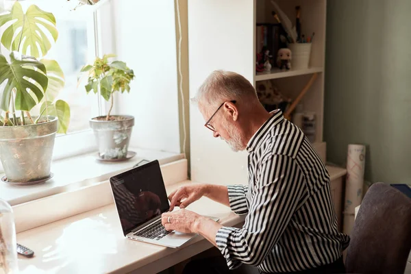 Mature bearded man working from home with laptop. sitting at desk near window — Stock Photo, Image