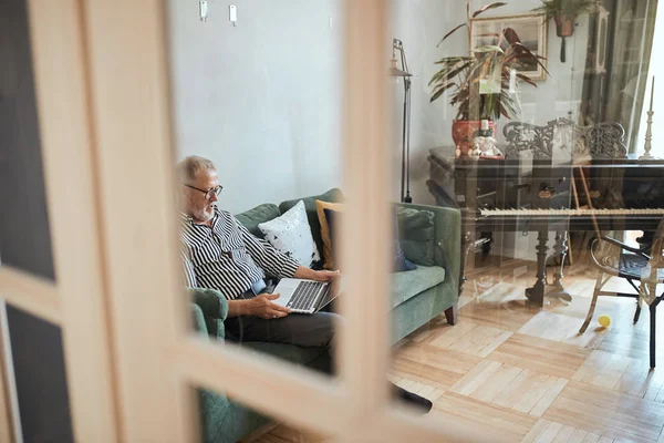 Hombre barbudo maduro que trabaja desde casa con el ordenador portátil. sentado en el escritorio cerca de la ventana — Foto de Stock