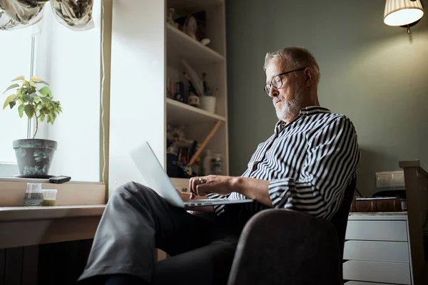 Mature bearded man working from home with laptop. sitting at desk near window — Stock Photo, Image