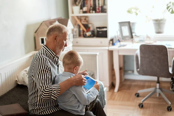 Abuelo y nieto usando tableta digital mientras están sentados en el sofá — Foto de Stock