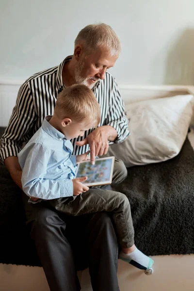 Dědeček a vnuk pomocí digitálního tabletu při sezení na gauči — Stock fotografie