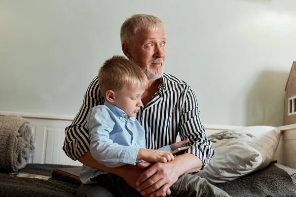 Abuelo y nieto usando tableta digital mientras están sentados en el sofá —  Fotos de Stock