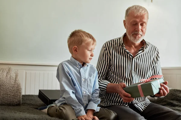 Generación. abuelo y nieto con caja de regalo sentado en el sofá en casa —  Fotos de Stock