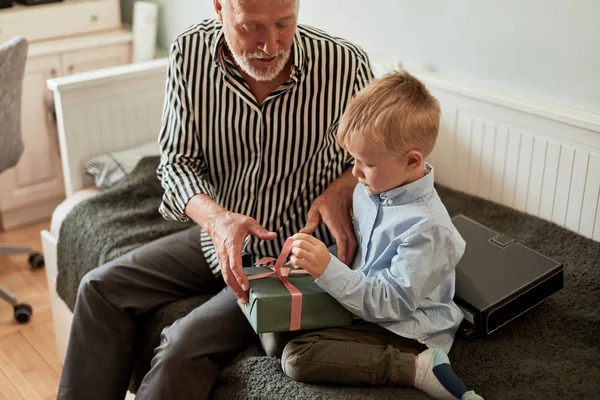 generation. grandfather and grandson with gift box sitting on couch at home