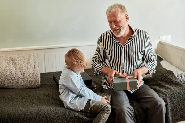 Generación. abuelo y nieto con caja de regalo sentado en el sofá en casa —  Fotos de Stock