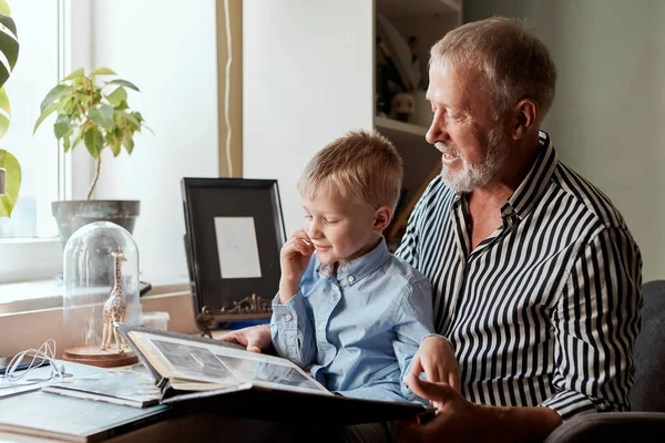 Grootvader en kleinzoon op de bank thuis. Opa en kinderen kijken naar oude foto 's — Stockfoto