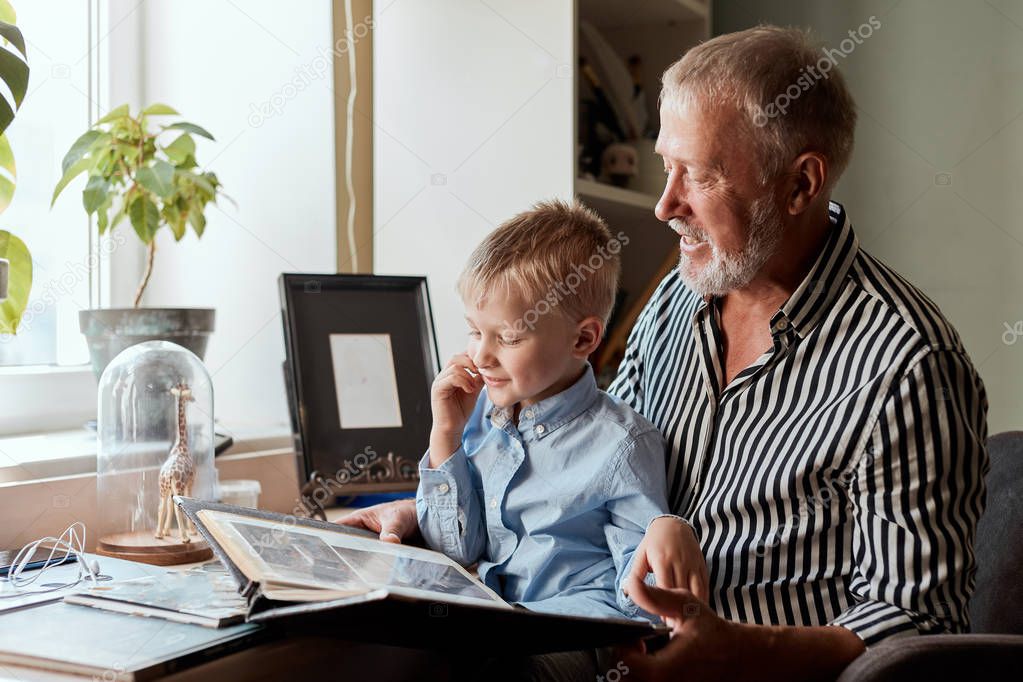 Grandfather and grandson on sofa at home. Grandpa and children watching old photos