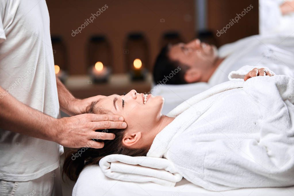 Beautiful young woman receiving massage on head and shoulders zone in spa centre