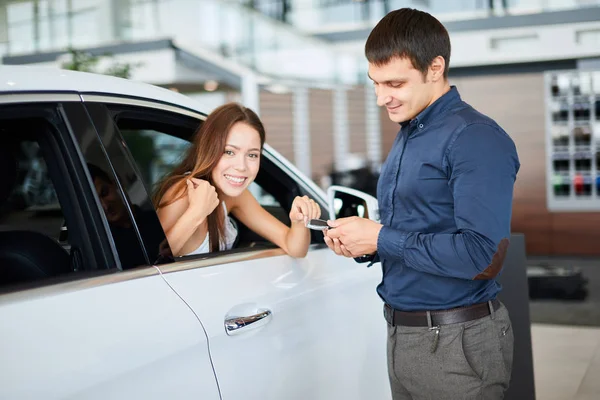 Verkäufer übergibt Autoschlüssel an junge Frau, die im Auto im Autohaus sitzt — Stockfoto