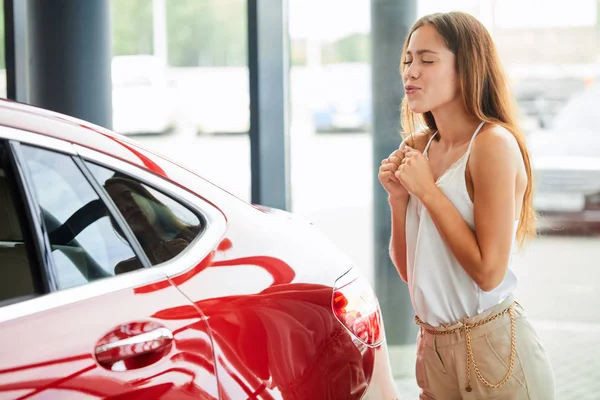 Zu Besuch bei einem Autohaus. Schöne junge Frau umarmt ihr neues Auto. — Stockfoto