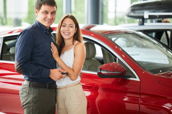 Happy loving couple embracing near their new luxury car at dealership. — Stock Photo, Image