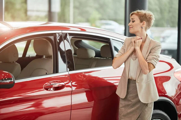 Feliz mujer caucásica abrazando su nuevo coche en la concesionaria de automóviles — Foto de Stock