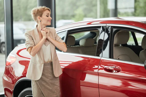 Feliz mujer caucásica abrazando su nuevo coche en la concesionaria de automóviles — Foto de Stock