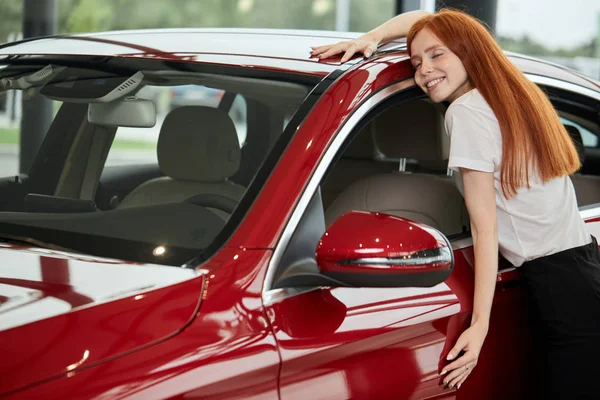 Heureuse femme caucasienne embrassant sa nouvelle voiture chez le concessionnaire automobile — Photo