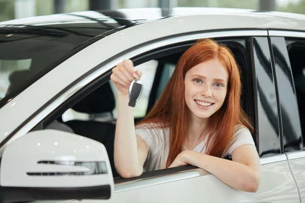 Overjoyed vezető nő mosolyog, és új kulcsot mutat, miközben ül az autó bemutatótermében — Stock Fotó