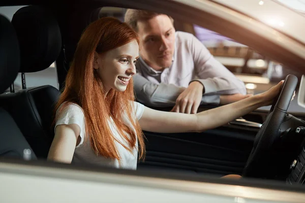 Молода щаслива жінка здивована новою машиною в автосалоні, подарунок від чоловіка — стокове фото