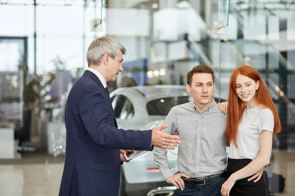 Feliz hermosa pareja está comprando un coche nuevo en la concesionaria. Consejo familiar — Foto de Stock