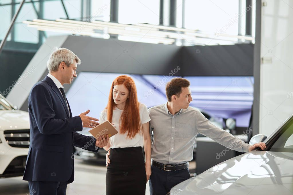 Car sales manager telling about the features of the car to the customers at the dealership