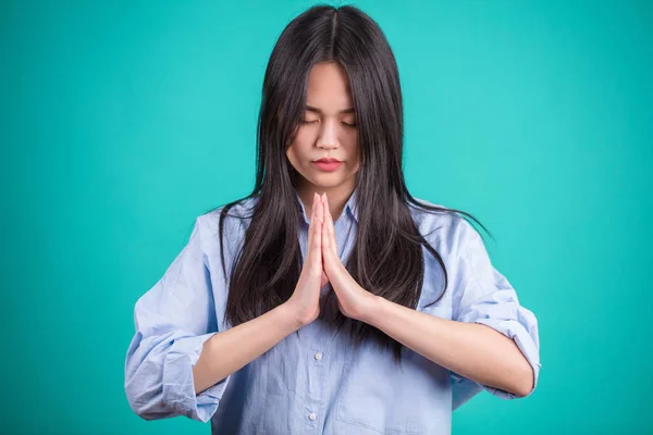 Азіатські молодій жінці молитися на тлі синього студії. — стокове фото