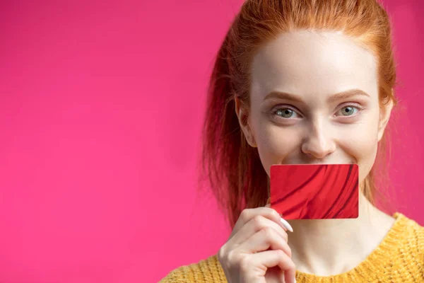 Feliz hermosa mujer de jengibre sosteniendo tarjeta de crédito aislada sobre fondo rosa . —  Fotos de Stock