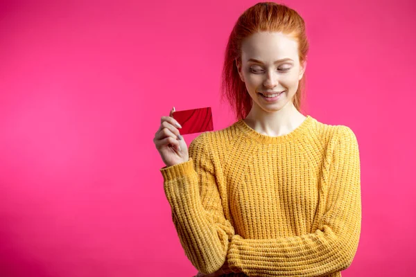 Feliz hermosa mujer de jengibre sosteniendo tarjeta de crédito aislada sobre fondo rosa . —  Fotos de Stock