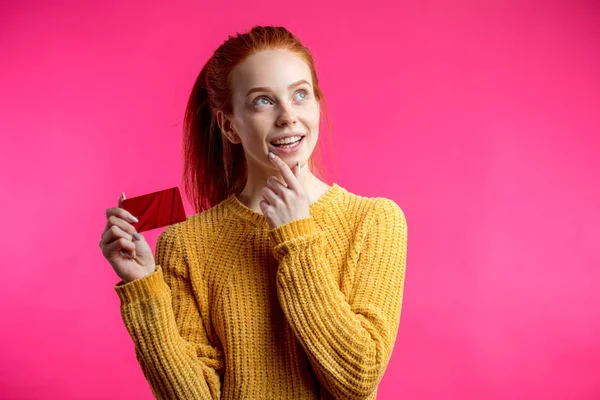 Feliz hermosa mujer de jengibre sosteniendo tarjeta de crédito aislada en pin — Foto de Stock