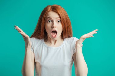 Uzun kızıl saçlı heyecanlı seyir sürpriz genç güzel kız ağzını açtı, holding baş, izole mavi yeşil duvar üzerinde eller. Sürpriz şok hayrete düşürdü. Olumlu insan duygu