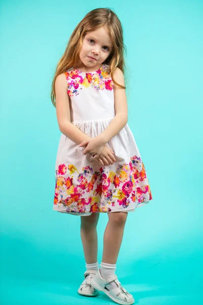 파란색 배경에 서 있는 긴 금발 머리와 아름 다운 작은 소녀 — 스톡 사진