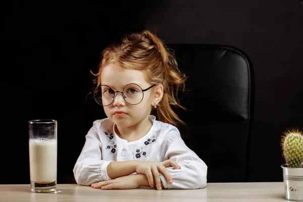 Menina sombria em óculos recusando-se a beber leite, sobre fundo preto — Fotografia de Stock