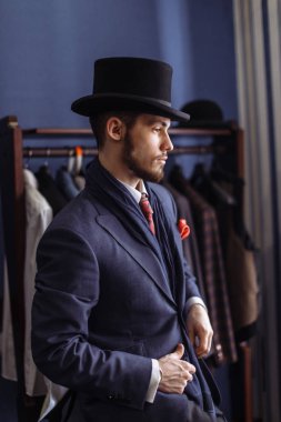 Portrait of attractive man in dark coat and trendy suit indoors tailors clipart