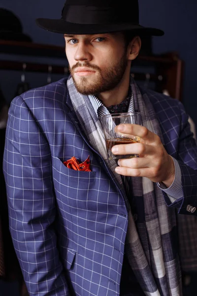 Hombre elegante en traje de moda y sombrero posando en el taller con bebida — Foto de Stock