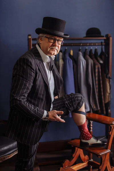 Fiducioso uomo di moda in stile retrò tirando su calzini su sgabello in legno sarti laboratorio — Foto Stock