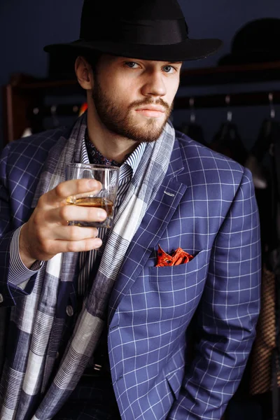 Elegant man in fashion suit and hat posing at atelier with beverage — Stock Photo, Image