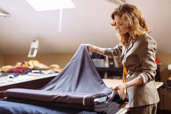 Женщина-модельер работает над подходящей тканью с аксессуарами для одежды на столе — стоковое фото