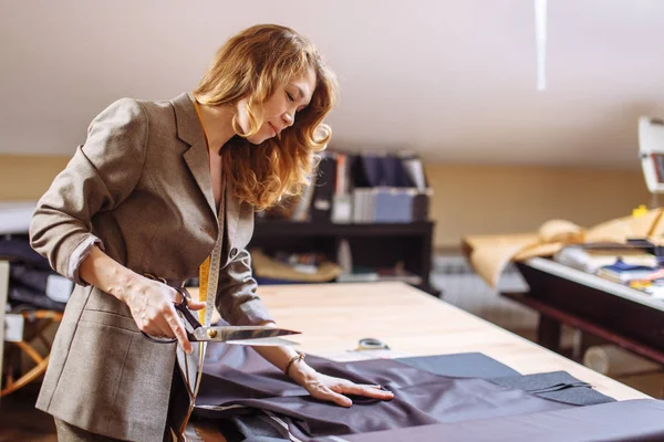 Diseñadora de moda femenina que trabaja en la tela adecuada con accesorios de confección en la mesa —  Fotos de Stock