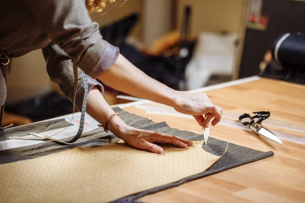 Профессиональная портная женщина маркирует ткань мелом в швейной мастерской и смотрит в камеру — стоковое фото