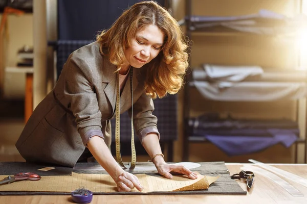 Профессиональная портная женщина маркирует ткань мелом в швейной мастерской и смотрит в камеру — стоковое фото