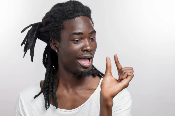 Homem de pele escura mostrando pequena coisa enquanto sorrindo e de pé perto de fundo branco — Fotografia de Stock