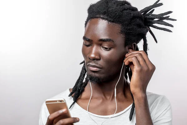 Afrykanin nosi słuchawki i trzyma smartfona na białym tle — Zdjęcie stockowe