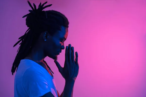 Close-up van zwarte man met dreadlocks bidden op paarse achtergrond — Stockfoto