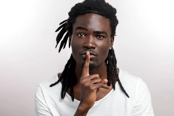 Joven de piel oscura gestos como secreto sosteniendo su dedo índice en sus labios, diciendo Shh — Foto de Stock