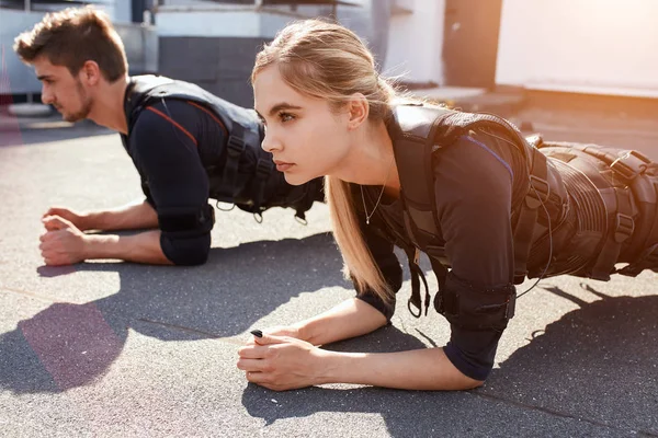 two young hardworking people are leaning on their elbows and doing exercises with ems device. health care, wellness concept. close up photo.