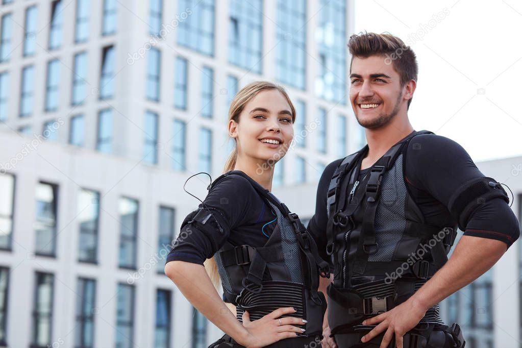 two positive young people wearing ems fitness vest and posing to the camera