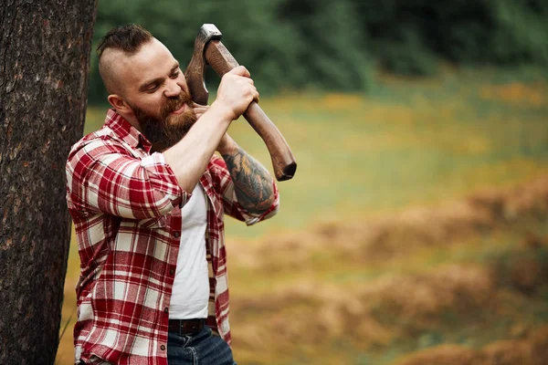 Mannen skogshuggare med skägg och mustasch i röd rutig skjorta rakar med yxa bladet på naturlig bakgrund — Stockfoto