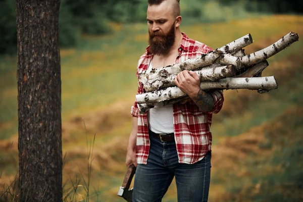 Bearded Man with firewoods and with axe on shoulder — Stock Photo, Image