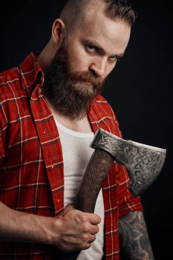 bearded male holding axe and posing in studio clipart